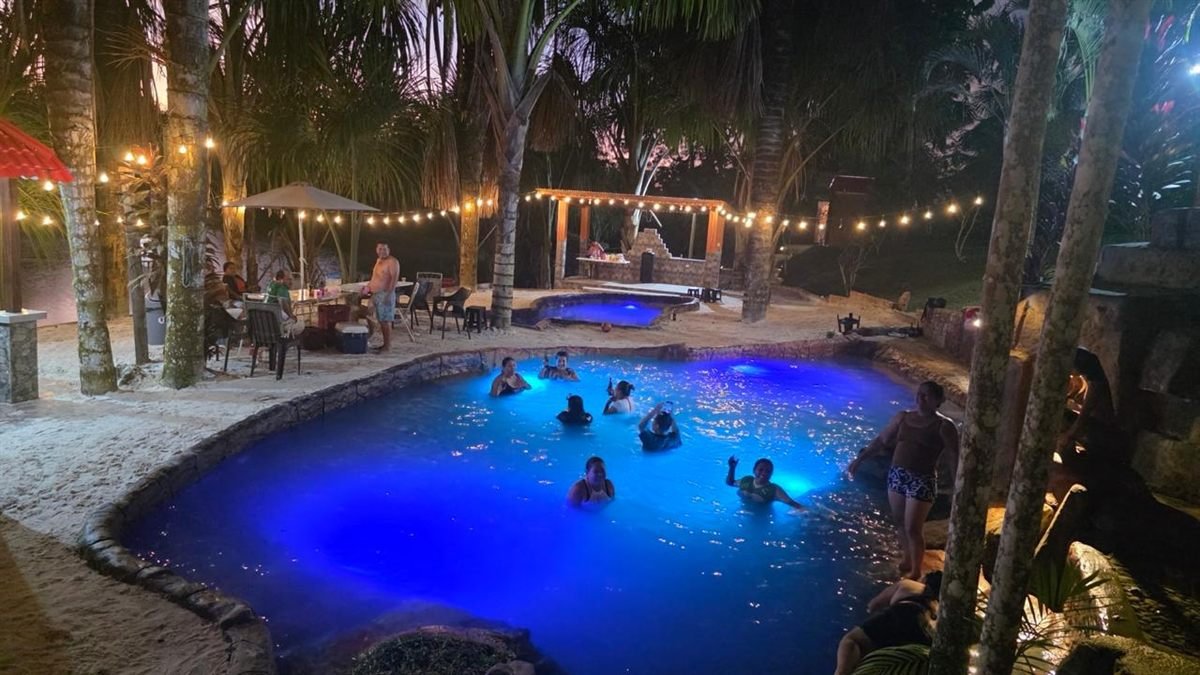 La piscina iluminada de noche, con visitantes bañándose y luces colgantes